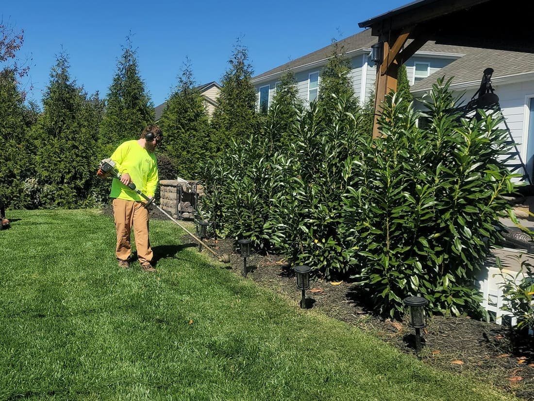 A two-person crew mowing and edging a large residential lawn.