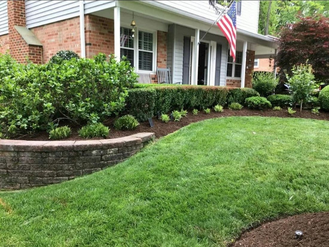 A front yard with a stone retaining wall, fresh mulch beds and trimmed shrubs.