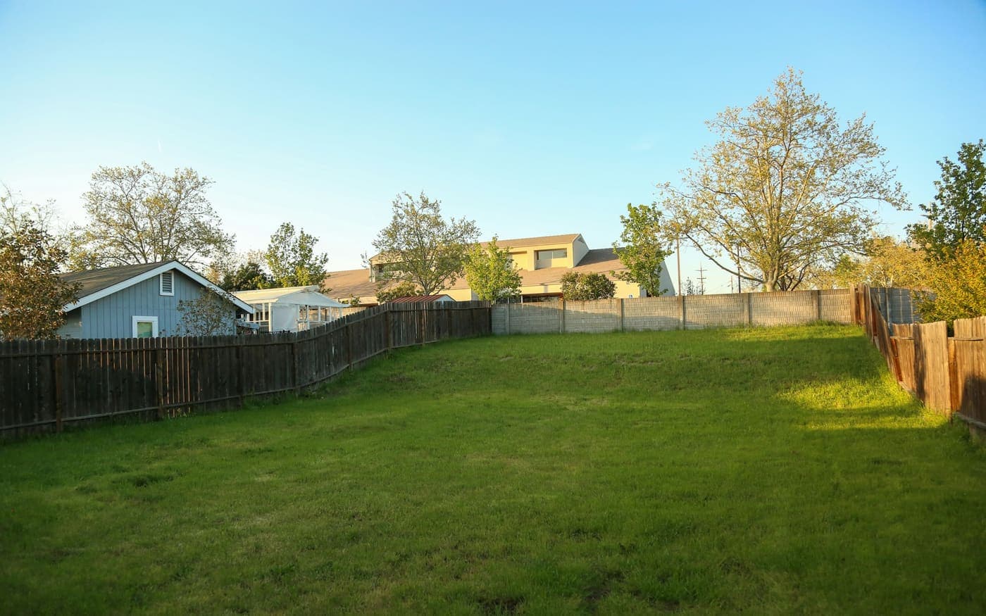 A fenced back yard in a western neighborhood under a clear blue sky.